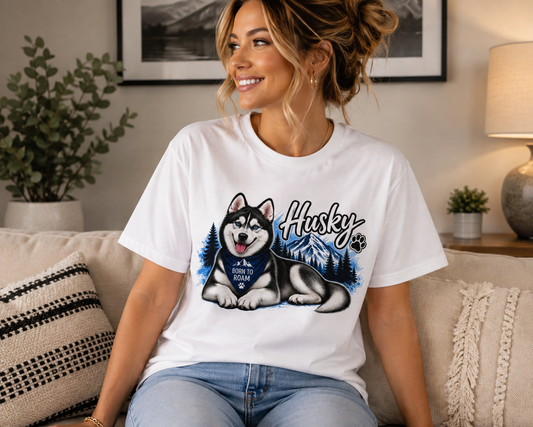 A woman sitting on a beige couch wearing a white graphic t-shirt with a husky illustration and the text 'Husky' and 'All Dogs Are Equal'.